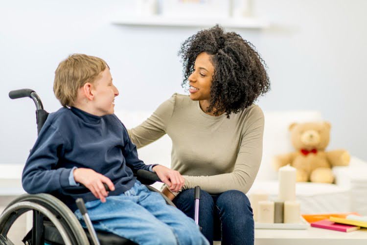 Caregiver sitting with a young client in a wheelchair in a bright home setting